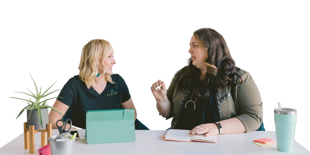 Ann-Rachel-Logo-Frame-03 Anne and Rachel, founders of RADZ Group, sitting at a desk talking to each other.